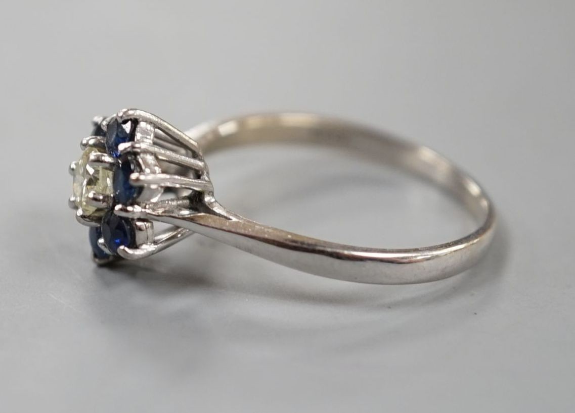 A modern 18ct white gold, single stone diamond and six stone sapphire set flower head cluster ring, size R, gross weight 3.7 grams.